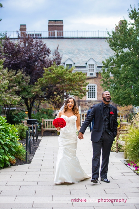 African american bride and groom in black suit and black shirt with red rose corsage with bride walking and laughing together during Nassau inn wedding princeton New Jersey