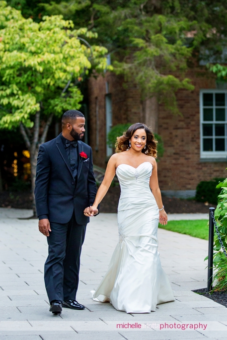 African american bride and groom in black suit and black shirt with red rose corsage with bride walking together during Nassau inn wedding princeton New Jersey