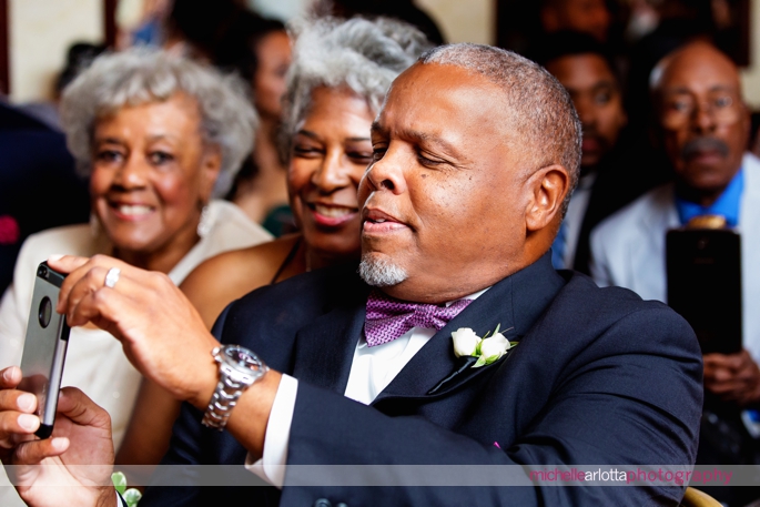 parents of the groom take a picture of groom as bride begins to walk down the aisle during indoor wedding ceremony at Nassau Inn in Princeton, New Jersey photographed by michelle Arlotta photography