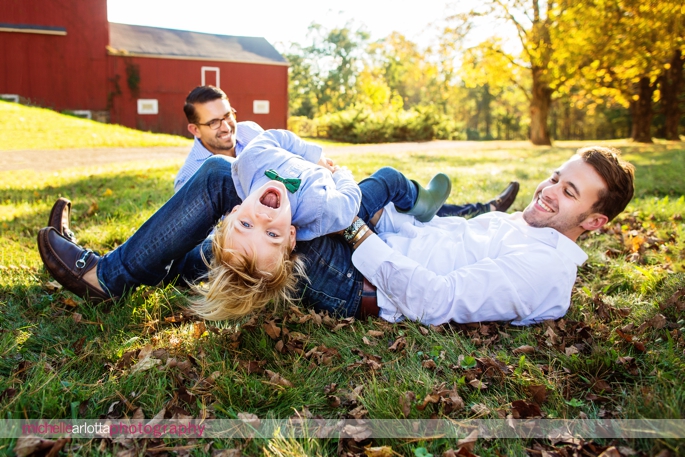 toddler plays around on his two dads like a jungle gym during candid family photography session in New Jersey