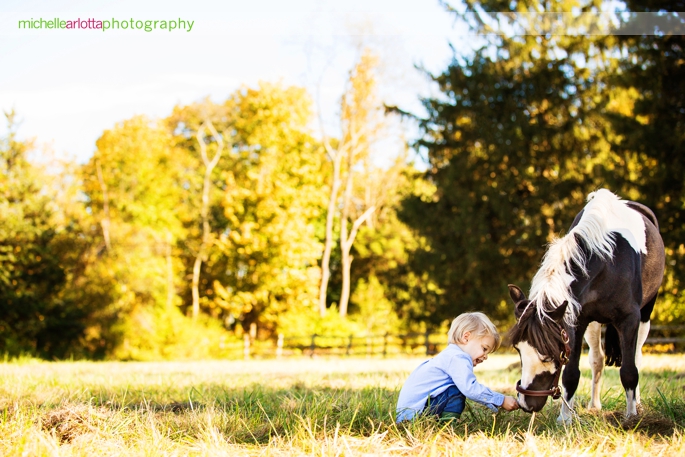 toddler with bowtie and hunter boots plays with his horse during candid family photography session in Bedminster, New Jersey