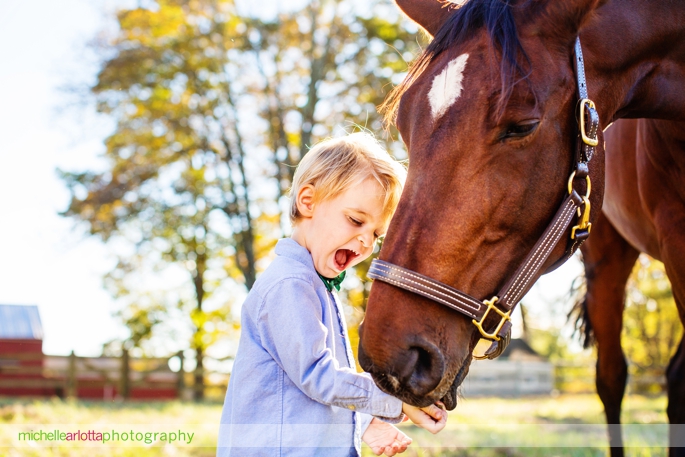 toddler laughs and smiles while feeding his horse during candid family photography session in Bedminster, New Jersey