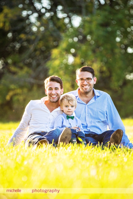 toddler with his two dads smile for the camera during family photography session
