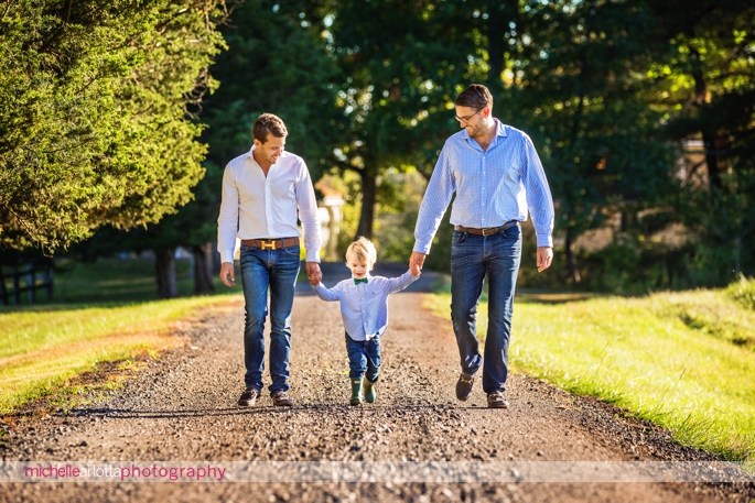 toddler with his two dads walking and holding hands on their long driveway in Bedminster, New Jersey during a candid family photography session
