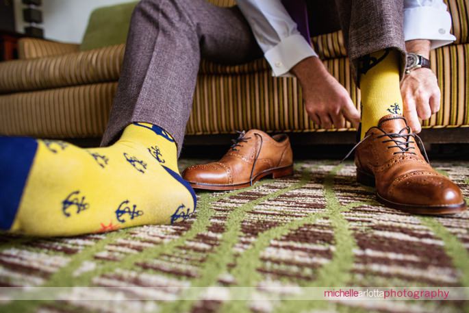 groom wearing yellow socks with blue anchors puts on brown shoes