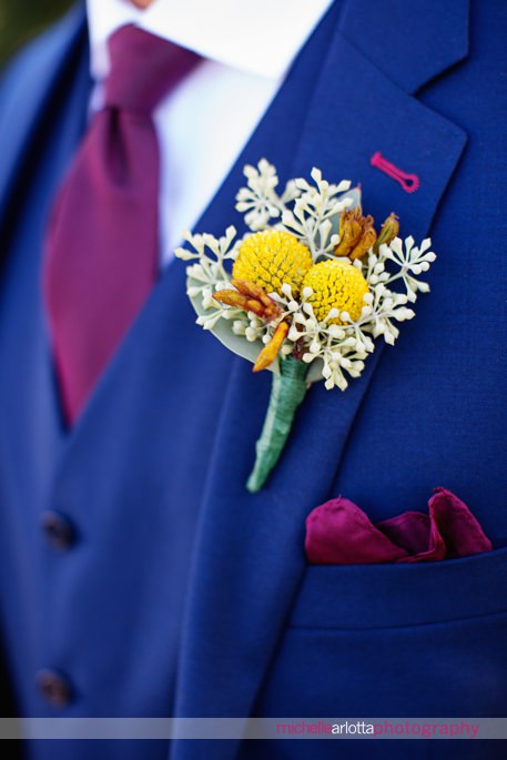 detail of groom's yellow boutonnière against blue suit with maroon tie by the garden state flower market