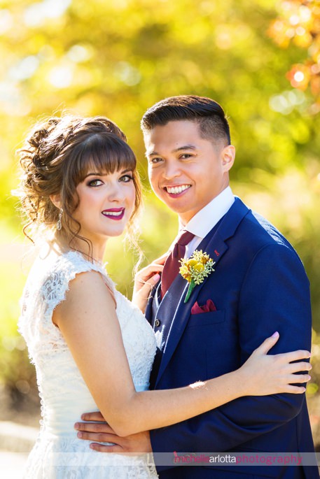 groom in blue suit with maroon detailing and bride in 3graces bridal wedding dress smile for a portrait at New Jersey's battleground country club