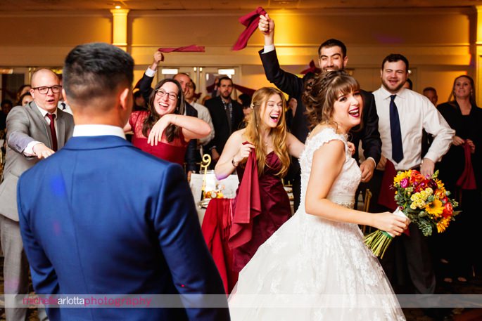 guests wave maroon napkins in the air as bride and groom enter wedding reception in Monmouth county, New Jersey