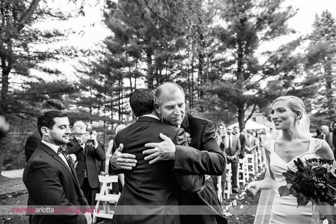 father of the bride hugs groom at altar at America's oldest winery, brotherhood outdoor wedding ceremony