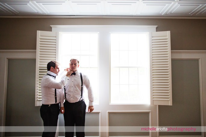 best man in suspenders helps groom get ready on wedding day in Sparta, new jersey