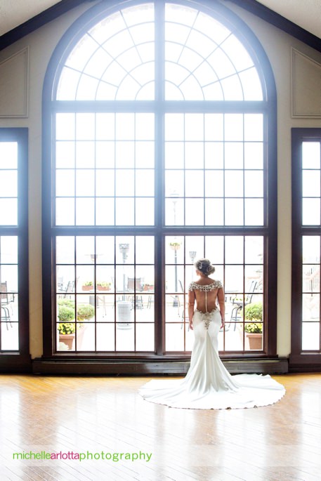 bride stands in front of giant window for portrait showing open back wedding dress during her lake mohawk country club wedding