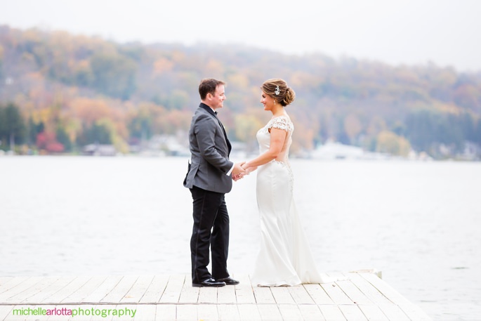 bride and groom stand on dock holding hands for their lake mohawk country club wedding in new jersey photographed by michelle Arlotta photography