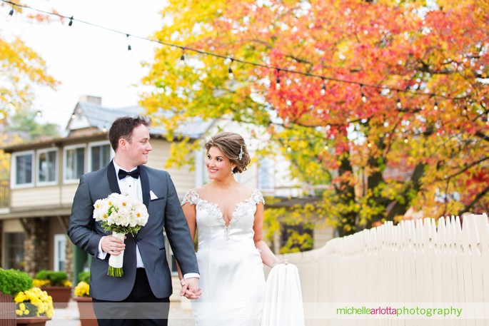 bride and groom walk along boardwalk at lake mohawk during their fall wedding day in Sparta New Jersey