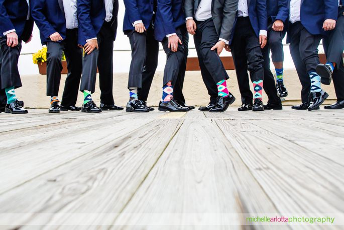 groomsmen in blue suits show off their different colorful socks on lake mohawk boardwalk