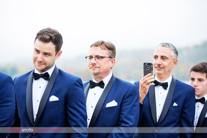 groomsmen in blue suits watch wedding ceremony on lake mohawk boardwalk