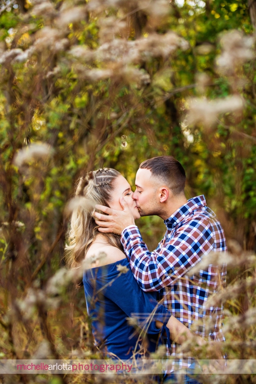 New Jersey wedding photographer captures groom grabbing bride's face and kissing her during fall engagement session in Frenchtown