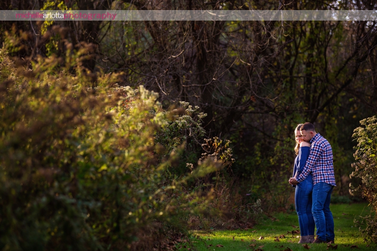 couple hugs one another in dramatic light during New Jersey golden hour engagement session in Frenchtown, New Jersey