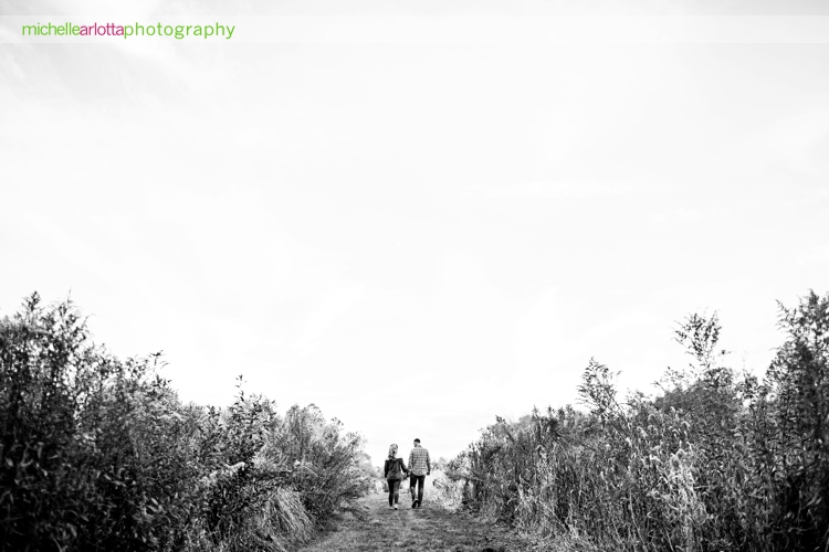 couple holds hands and walks among fields in wide angle shot by New Jersey wedding photographer michelle Arlotta