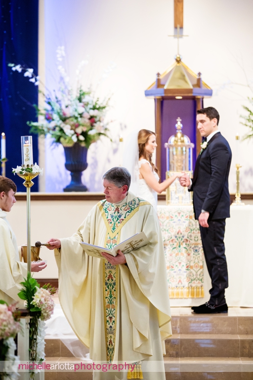 priest blesses rings during wedding ceremony at st. Elizabeth Ann seton three bridges church