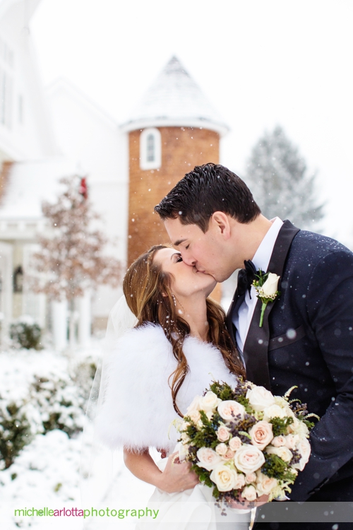 bride and groom kiss at landmark venues Ryland inn coach house silo in background during snowy winter wedding