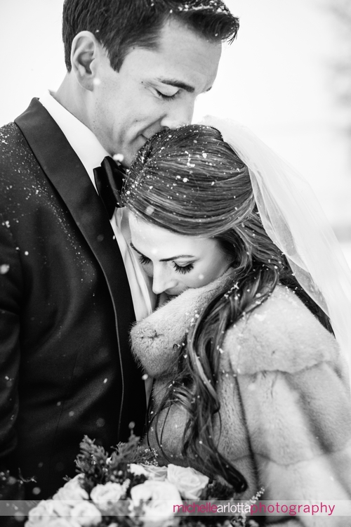bride and groom snuggle during portraits at Ryland inn coach house silo in background during snowy winter wedding with New Jersey wedding photographer Michelle Arlotta photography