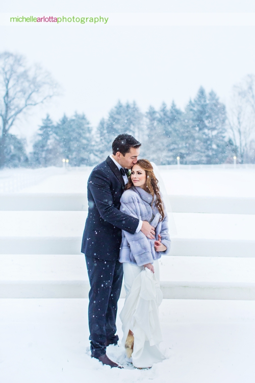 bride and groom cuddle together in snow during portraits at Ryland inn coach house winter wedding with New Jersey wedding photographer Michelle Arlotta photography
