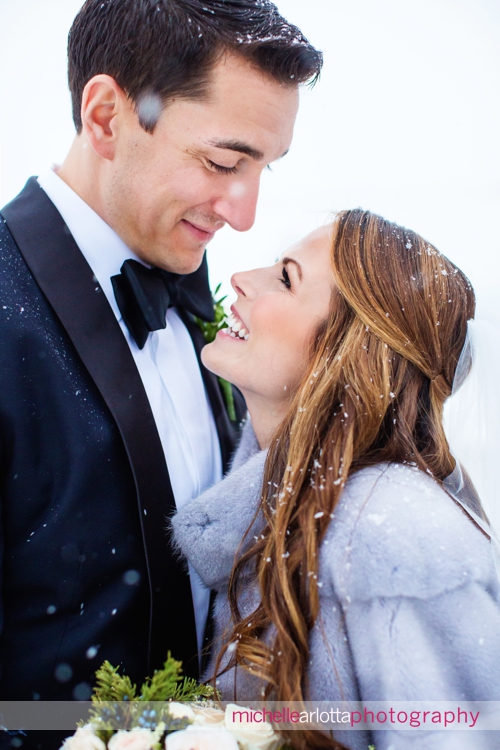bride and groom smiling at one another in snow during portraits at Ryland inn coach house winter wedding with New Jersey wedding photographer Michelle Arlotta photography
