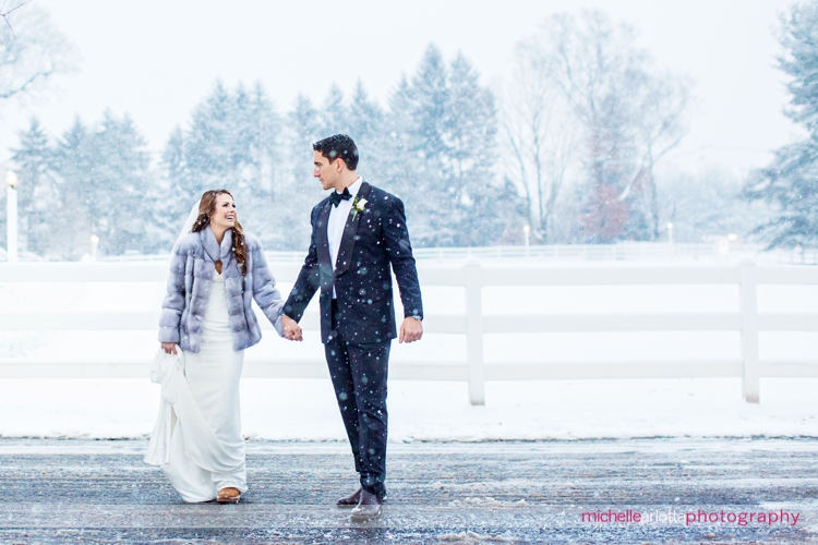 bride and groom walk holding hands in snow during portraits at Ryland inn coach house winter wedding with New Jersey wedding photographer Michelle Arlotta