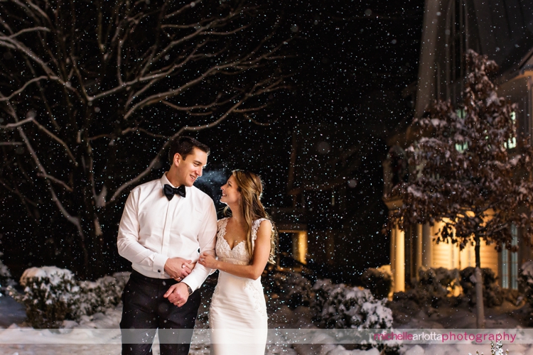 bride in chiarade wedding dress walks with groom during snowy nightshot at their Ryland inn coach house winter wedding photographed by New Jersey wedding photographer michelle arlotta