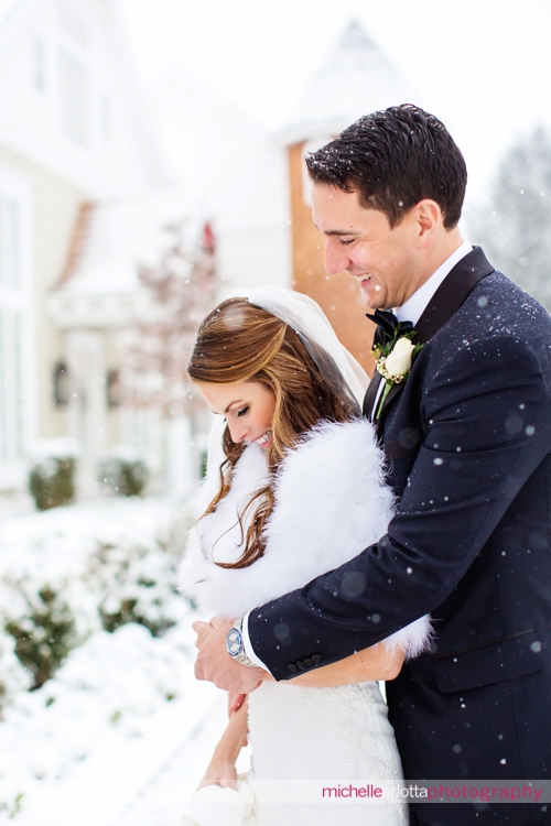 bride with white fur candidly laughs with groom in tux during Ryland inn coach house winter wedding portraits