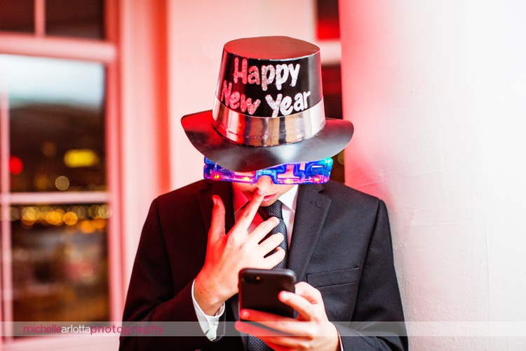 kid wear's happy new year hat and light up glasses while on phone during new year's eve wedding reception at New Jersey wedding