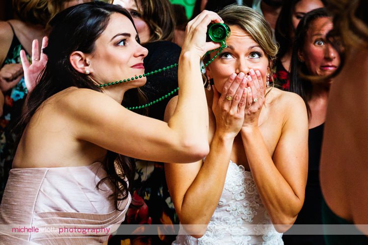 bride covers her mouth and makes silly face as bridesmaid pours from empty tiny green mug