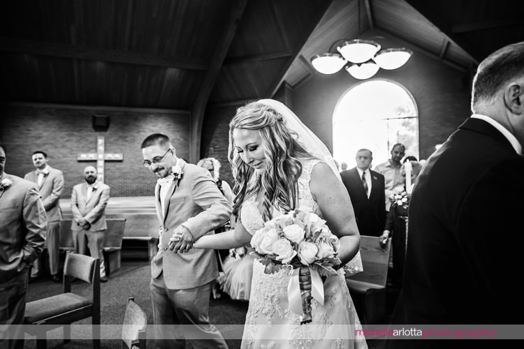 bride and groom hold hands and walk up to altar during wedding ceremony at St Charles Borromeo Church in skillman, NJ