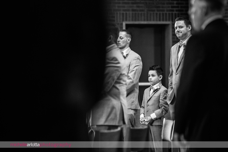 ring bearer in grey suit stands during wedding ceremony at St Charles Borromeo Church in skillman, NJ