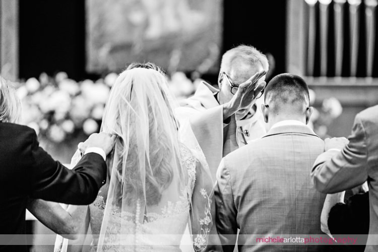 parents at altar with bride and groom for blessings during wedding ceremony at St Charles Borromeo Church in skillman, NJ