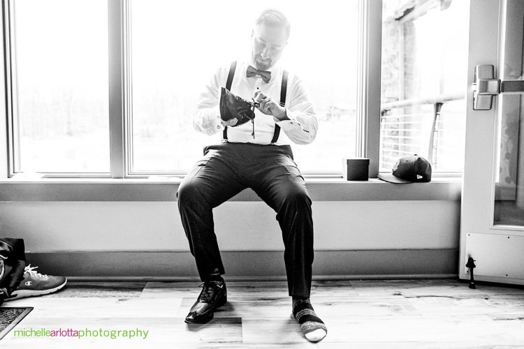 groom in suspenders puts on his shoes
