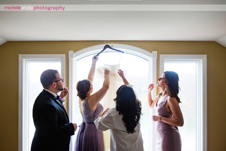 bride and her bridal party get her the white gown down from the window