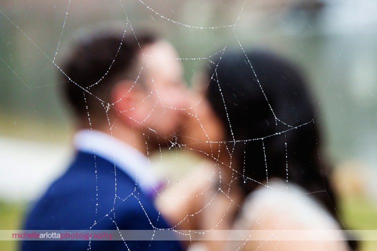 bride and groom kiss with spider web with rain on it in the foreground