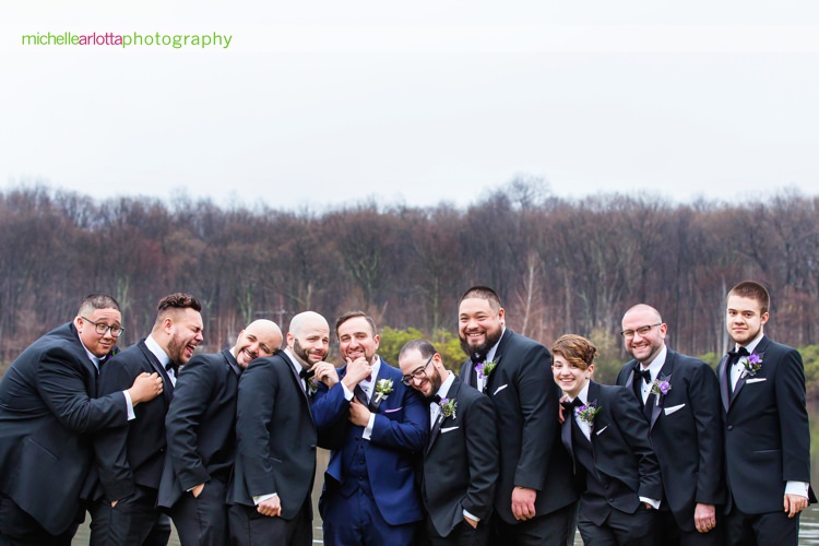 groom in blue suit and groomsmen in black suits huddle together for a pick at rock island lake club spring wedding