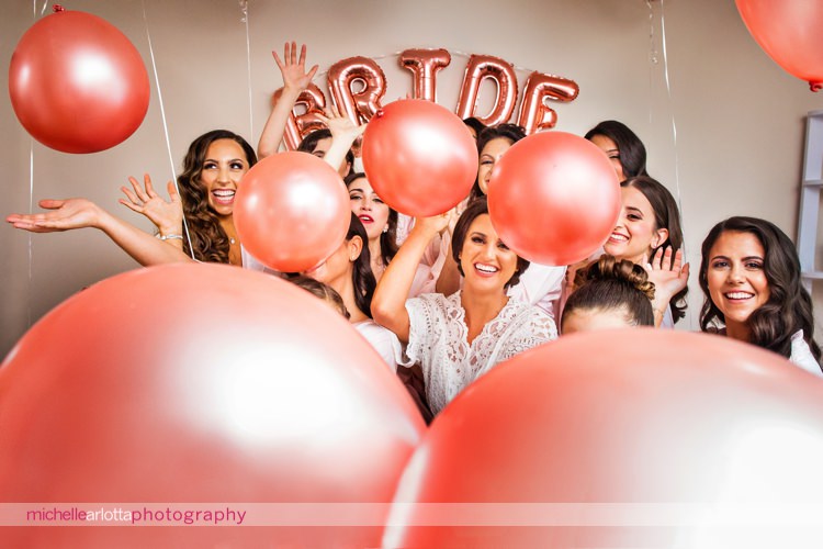 bride in lace robe and bridesmaids in floral robes throw pink balloons at camera