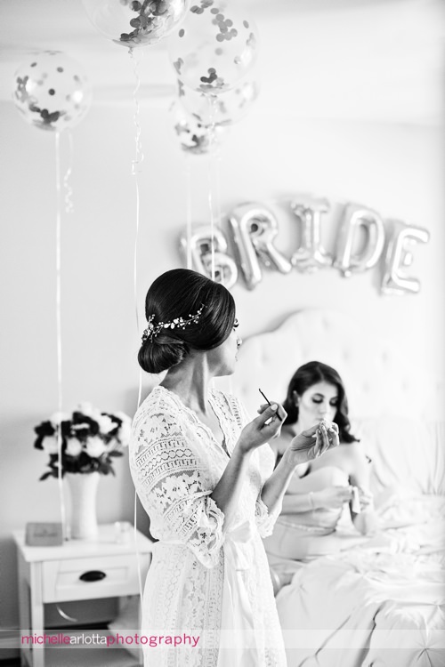 bride in lace robe puts on lip gloss in her room with bride balloons on the wall