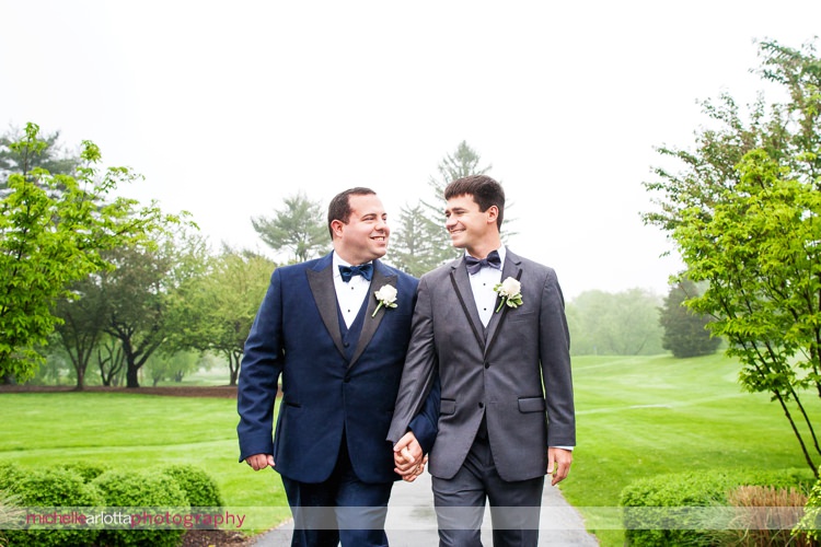 groom in midnight blue suit and groom in grey suit walk hand in hand at rockaway river golf club
