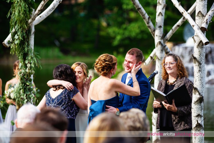 mothers embrace the bride and groom at altar during outdoor lakeside nj wedding ceremony
