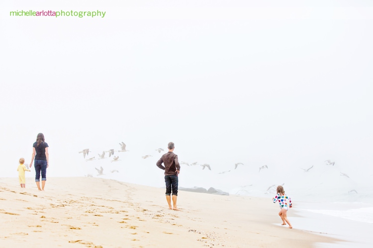 family of four watches as seagulls flock in the fog at the New Jersey shore