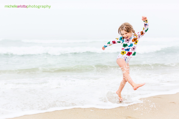 little girl kicks up water and smiles in joy at asbury park nj beach