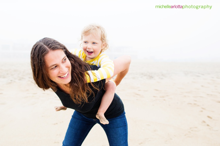 toddler piggybacks on her mother at the nj shore for family photography session