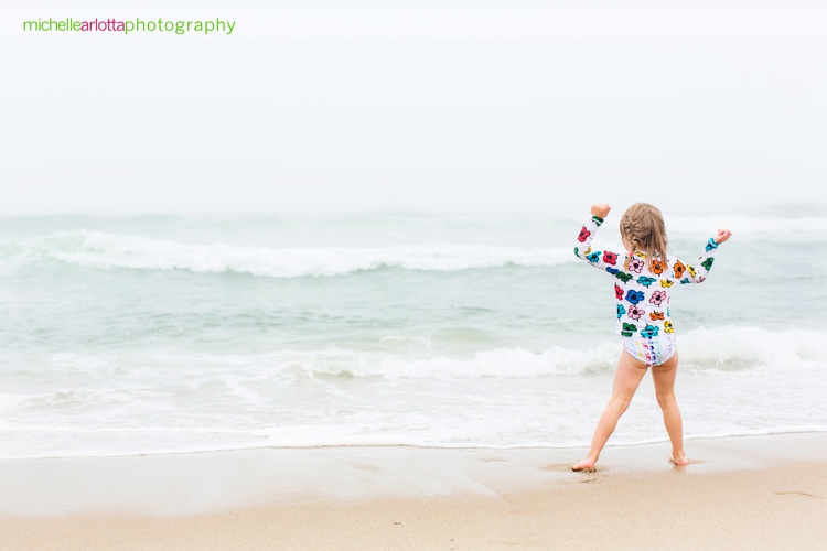 little girl enjoys the water on a foggy day during New Jersey shore family photo sessions with candid lifestyle photographer Michelle arlotta