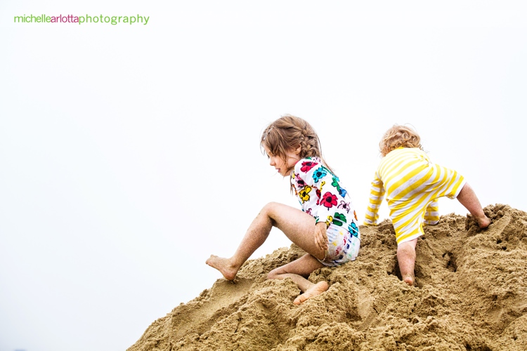 sisters climb giant sand mound during New Jersey beach family session with Michelle arlotta photography