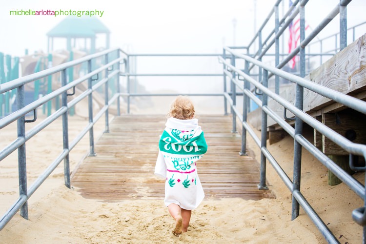 toddler wrapped up in towel walks up to boardwalk on a foggy day after New Jersey family photo session with Michelle arlotta photography
