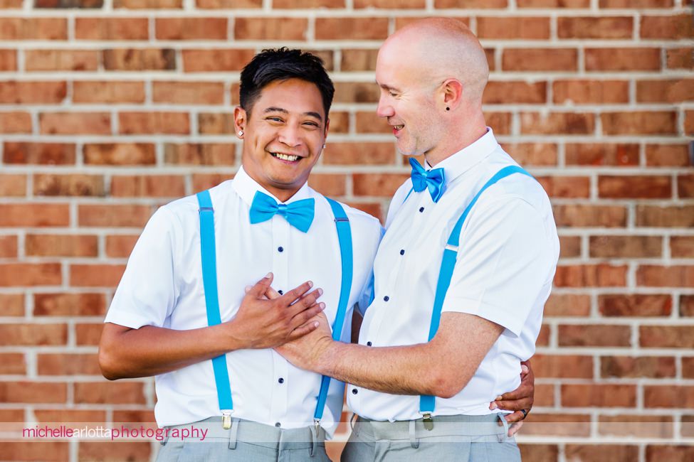 two grooms in blue bowties and blue suspenders smile together in cape may